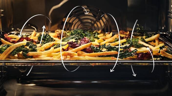 French fries and vegetables are being prepared in an oven.